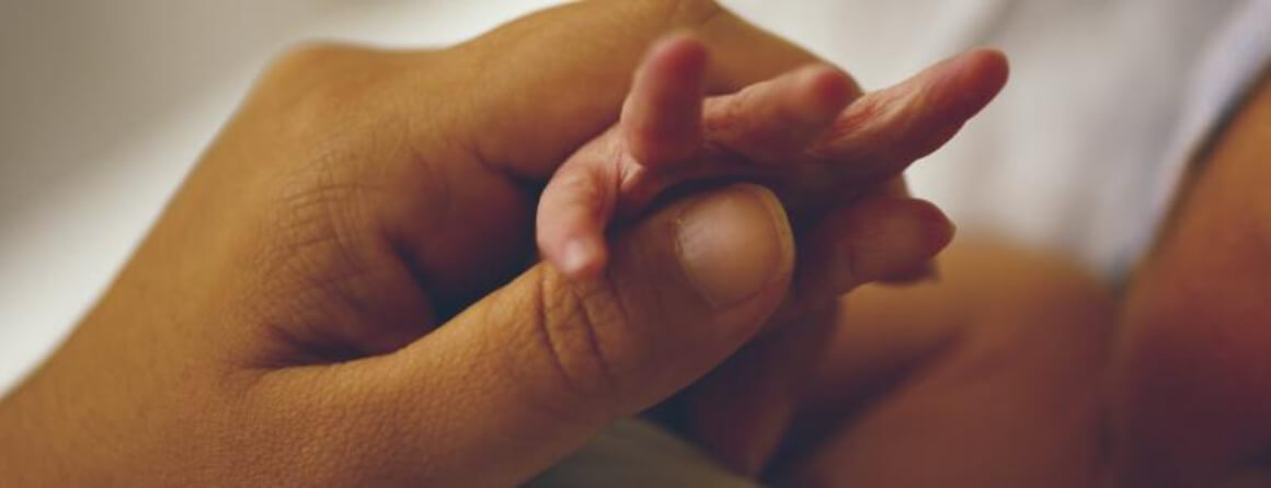 Womans hand holding the hand of a newborn infant